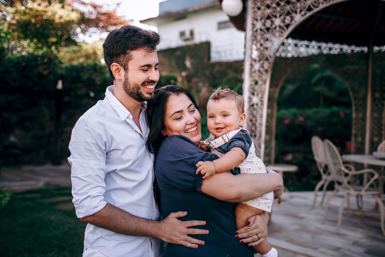 Smiling parents holding their baby in an outdoor garden setting, spending quality time together.